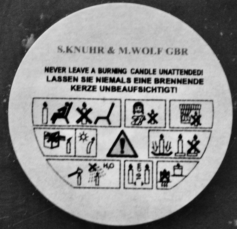 May include: Black and white warning label with the text "S.KNUHR & M.WOLF GBR" and "NEVER LEAVE A BURNING CANDLE UNATTENDED! LASSEN SIE NIEMALS EINE BRENNENDE KERZE UNBEAUFSICHTIGTI" along with several safety pictograms.