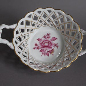 May include: White porcelain bowl with a delicate openwork design and a pink floral motif. The bowl has two handles and is perfect for serving fruit or snacks.