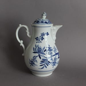 May include: A white porcelain coffee pot featuring a blue floral pattern painted on the exterior. The pot includes a matching lid with a small finial, a curved handle, and a spout. The design consists of delicate blue botanical motifs.