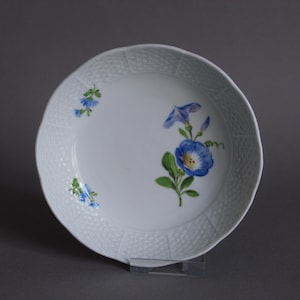 May include: White ceramic plate with a scalloped edge and a textured rim. The plate is decorated with hand-painted blue morning glory flowers and green leaves. A smaller cluster of blue flowers is on the left side.