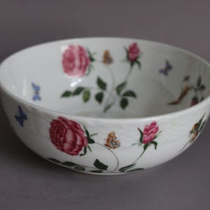 Puede incluir: Cuenco de cerámica blanca con diseño floral de rosas rosas, hojas verdes y mariposas. El cuenco tiene una superficie texturizada y una forma ancha y poco profunda, ideal para servir o decorar. Diámetro aproximado de 25 cm.