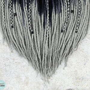 May include: Gray and black ombre synthetic dreadlocks with black beads. The dreadlocks are arranged in a heart shape.