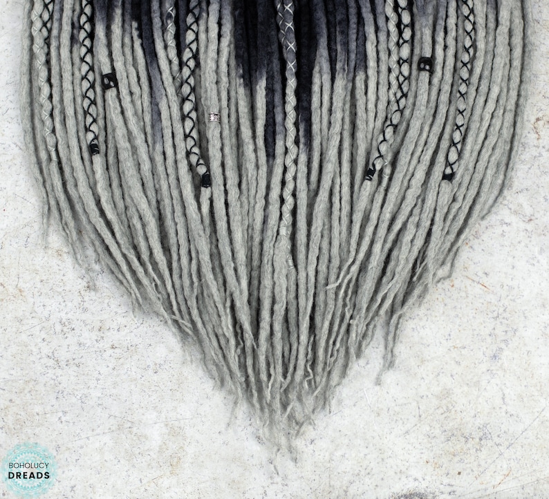 May include: Gray and black ombre synthetic dreadlocks with black beads. The dreadlocks are arranged in a heart shape.