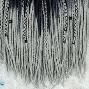 May include: Gray and black ombre synthetic dreadlocks with silver and black beads. The dreadlocks are approximately 24 inches long.