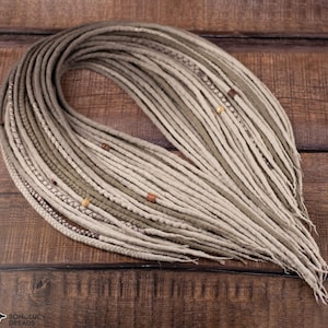May include: A set of synthetic dreadlocks in shades of beige, tan, and light brown. The hair extensions feature various textures, including smooth, braided, and wrapped strands, accented with small wooden beads throughout the arrangement.