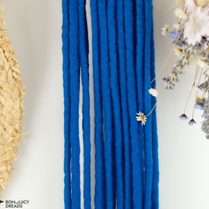 May include: Close-up of blue and white synthetic dreadlocks. The dreadlocks are made of soft, fuzzy material and are arranged in a straight line.