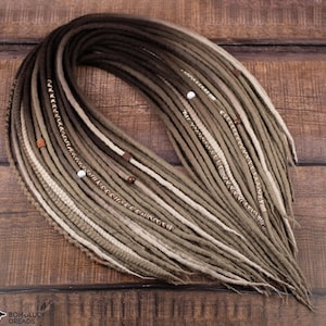 Può includere: Un fascio di dreadlock fatti a mano nei toni del marrone, beige e crema. I dread sono adornati con piccole perline di legno e perline bianche. I dreadlock sono disposti su una superficie di legno.
