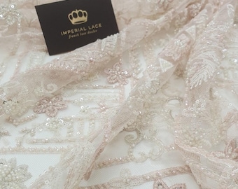 May include: Close-up of delicate, beaded lace fabric in a blush pink colour. The lace features intricate floral designs and small, sparkling sequins. The fabric is soft and flowing, with a subtle sheen. The text "IMPERIAL LACE French lace dealer" is visible in the top left corner of the image.