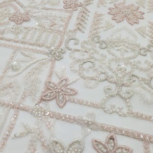 May include: White and pink beaded fabric with a geometric pattern. The fabric is made of a sheer mesh material and is decorated with small beads and sequins.