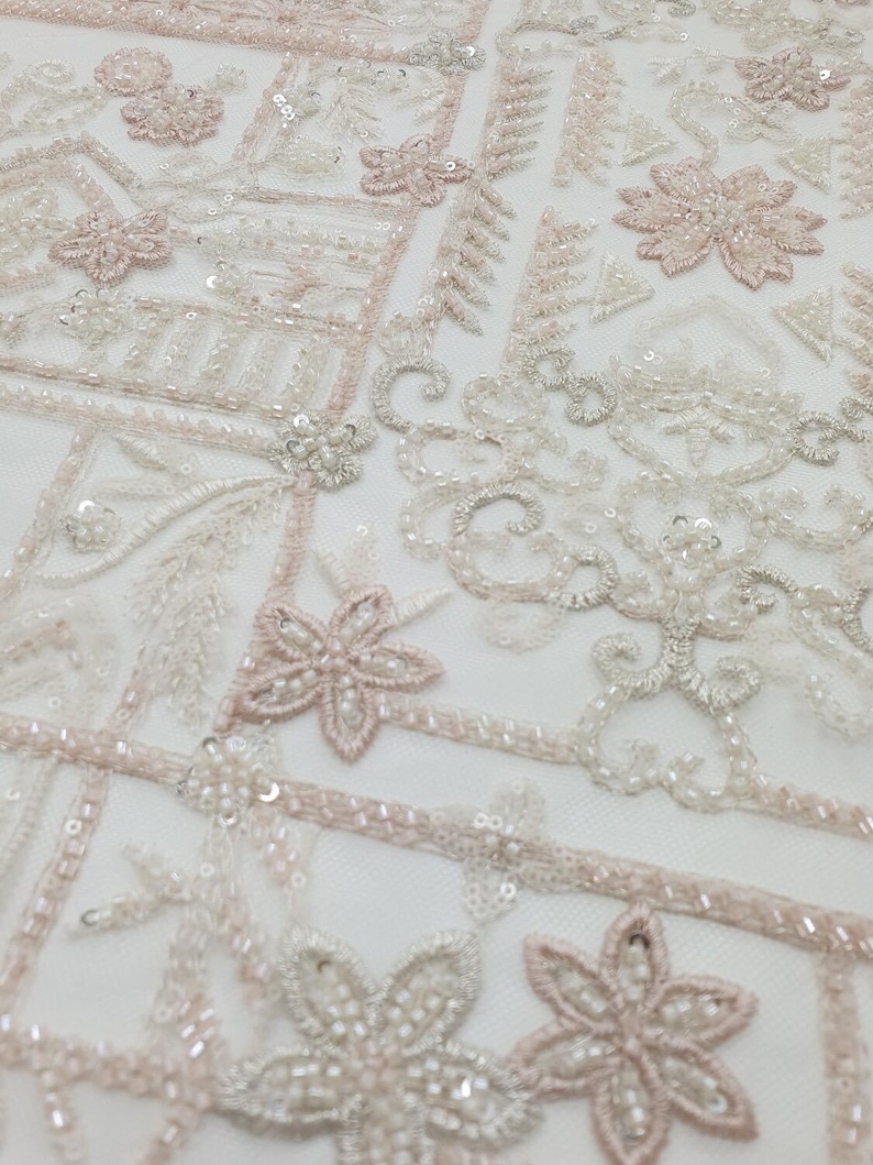 May include: White and pink beaded fabric with a geometric pattern. The fabric is made of a sheer mesh material and is decorated with small beads and sequins.