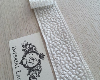 May include: White lace trim with a textured pattern. The trim is folded in half and the label "IMPERIAL LACE" is visible.