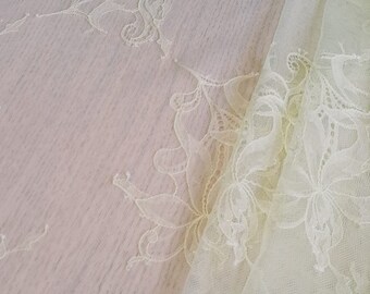 May include: A piece of delicate, off-white lace fabric with a floral pattern. The fabric is sheer and has a soft, flowing texture.
