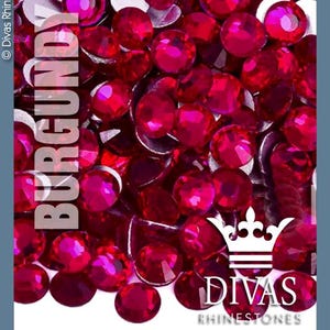 May include: A close-up image of a large quantity of small, round, burgundy red rhinestones. The rhinestones are scattered on a white surface. The text "BURGUNDY RED" is written vertically on the left side of the image. The text "DIVAS RHINESTONES" is written in white on a black crown logo in the bottom right corner of the image.