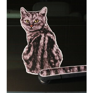 May include: A black and white cat sticker for a car window. The cat is looking back over its shoulder.