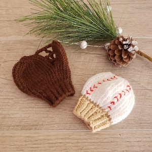May include: Two knitted baseball-themed hats. One is brown and shaped like a baseball glove, the other is white with red stitching and a tan brim.