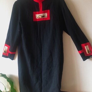 May include: A black dress with red and white trim and gold buttons. The dress has a mandarin collar and long sleeves.