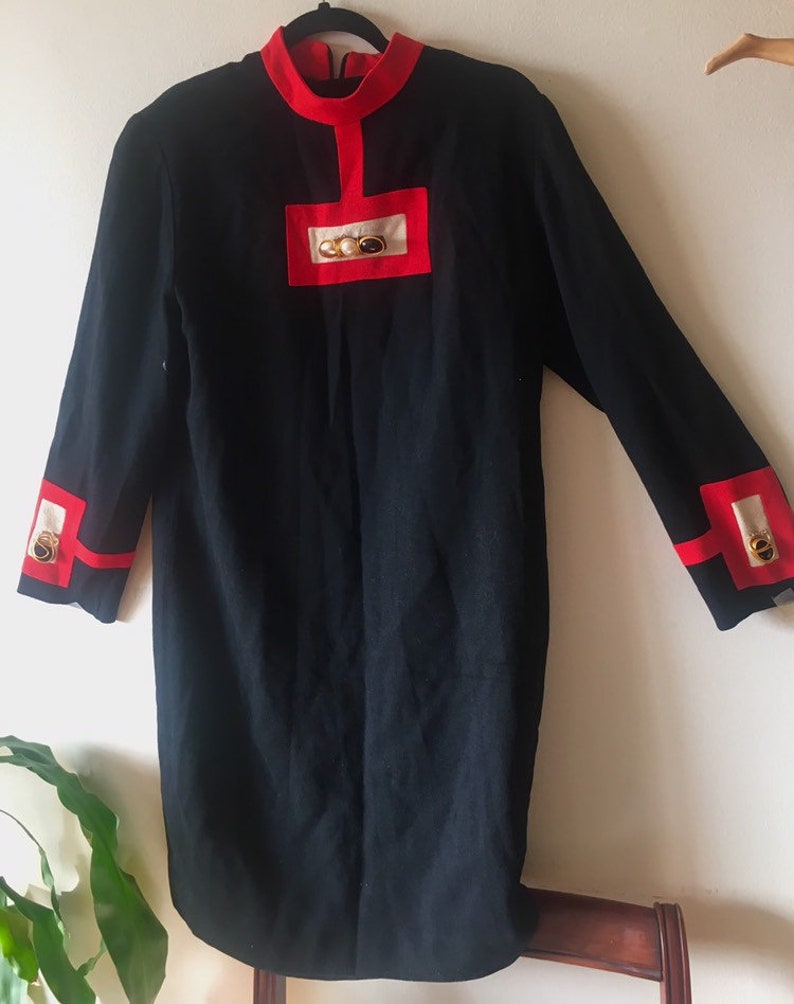 May include: A black dress with red and white trim and gold buttons. The dress has a mandarin collar and long sleeves.