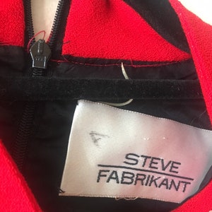 May include: Close-up of a black and red dress with a zipper and a white label that reads "STEVE FABRIKANT".