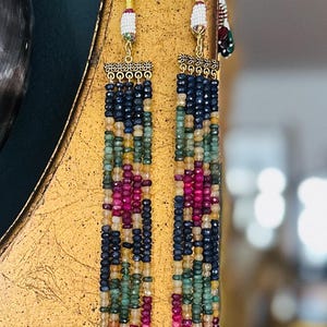 Puede incluir: Un collar de múltiples hilos con una variedad de piedras preciosas, incluyendo rubí, zafiro y esmeralda. El collar está hecho de oro y tiene un borla al final.