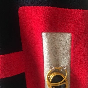 May include: A close-up of a red, white, and black fabric with a gold metal ring with a black stone in the center.