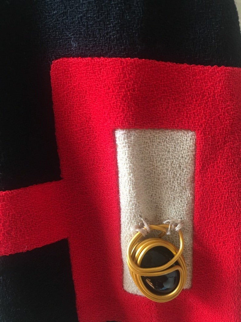 May include: A close-up of a red, white, and black fabric with a gold metal ring with a black stone in the center.