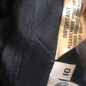 May include: A black wool garment with a white tag that says "IMPORTANT PLEASE HAVE YOUR DRY CLEANER REMOVE BUTTONS BEFORE DRY", "10", and "90% PURE WOOL REVERSE FOR CARE".