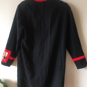 May include: A black dress with red trim around the collar and cuffs. The dress has a long sleeve and a zipper down the back.