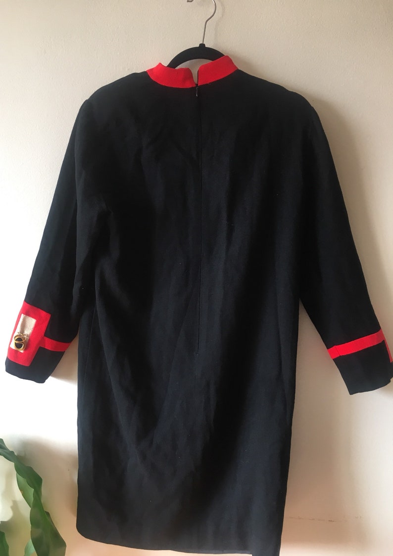 May include: A black dress with red trim around the collar and cuffs. The dress has a long sleeve and a zipper down the back.