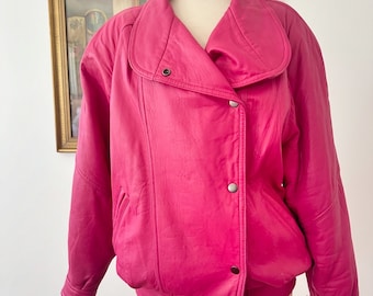Puede incluir: Chaqueta rosa brillante con cuello ancho y cierre de botones. La chaqueta se exhibe en un maniquí, mostrando su diseño. La chaqueta tiene un estilo bomber clásico con una silueta ligeramente abombada.