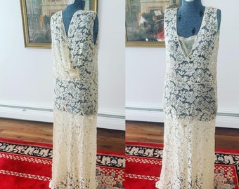 May include: A long, white lace dress with a V-neckline and a flowing skirt. The dress is sleeveless and has a delicate floral pattern.