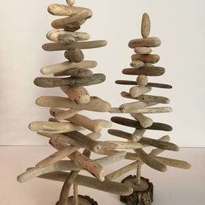 May include: Two driftwood Christmas trees, one taller than the other, are stacked with pieces of driftwood and placed on wooden bases.