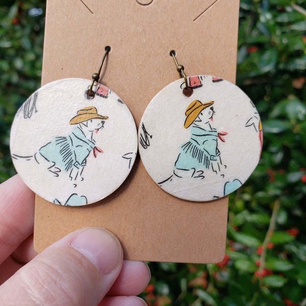 Cowboy dog Handmade wooden circle dangle earrings,  white dog wearing a jacket with fringe and handkerchief with brown cowboy hat