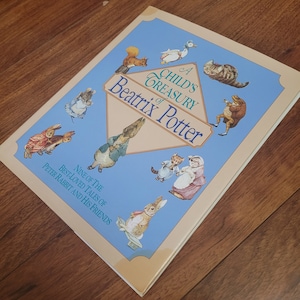 Puede incluir: Una cubierta de libro azul y crema con el título "A Child's Treasury of Beatrix Potter" e ilustraciones de personajes de los libros de Beatrix Potter, incluyendo Peter Rabbit, Jemima Puddle-Duck y Mrs. Tiggy-Winkle.