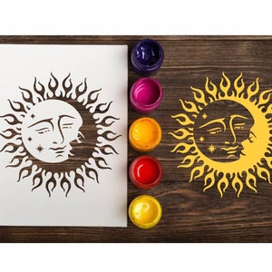 Peut inclure: Un pochoir blanc avec un motif de soleil et de lune noir. Le soleil et la lune ont des visages et sont entourés de flammes. Le pochoir est sur une surface en bois avec des pots de peinture.