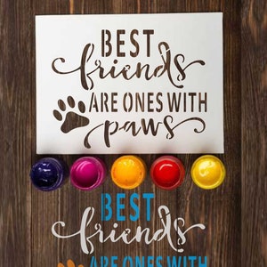 以下が含まれることがあります： 「Best friends are ones with paws」というテキストと肉球のプリントが書かれたステンシル。ステンシルは、青、ピンク、黄、赤、オレンジの塗料が入った缶が置かれた木製の表面の上に置かれている。