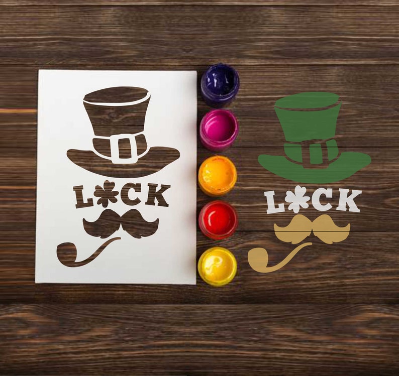 May include: A white stencil with a leprechaun hat, mustache, pipe, and the text "L*CK". The stencil is on a wooden surface with paint pots in various colors.