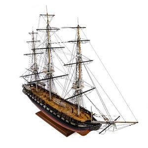 May include: A detailed wooden model of a tall ship, with multiple masts and intricate rigging. The ship has a black hull, a wooden deck, and is mounted on a wooden base. The model is a replica of a historical sailing vessel, showcasing fine craftsmanship.