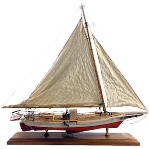 May include: A detailed model sailboat with a cream-colored sail and a red and white hull. The model is mounted on a wooden base and features intricate rigging and a small dinghy. The sailboat is a classic nautical decorative item.