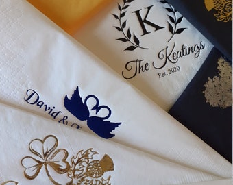 May include: A stack of white napkins with gold foil designs. The top napkin has a blue silhouette of two swans with the text "David &" above them. The second napkin has a gold shamrock and a gold thistle. The third napkin has a gold horse and rider. The fourth napkin has a black wreath with the letter "K" in the center and the text "The Keating's Est. 2020".