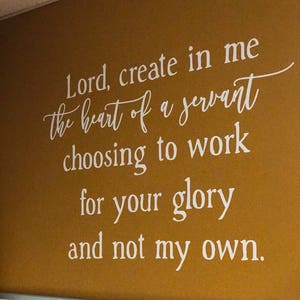 May include: A white wall with a motivational quote written in white lettering: "Lord, create in me the heart of a servant choosing to work for your glory and not my own."