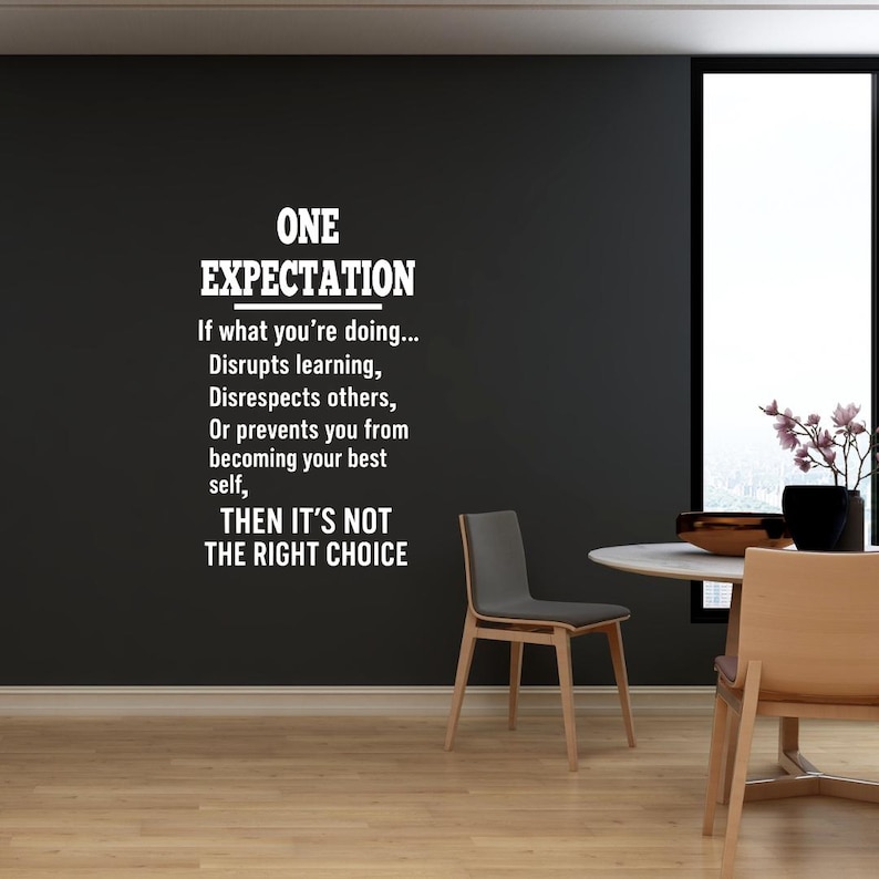 May include: A black wall with a white vinyl decal that reads "ONE EXPECTATION. If what you're doing... Disrupts learning, Disrespects others, Or prevents you from becoming your best self, THEN IT'S NOT THE RIGHT CHOICE."
