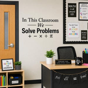 May include: A black wall decal with the text In This Classroom We Solve Problems and mathematical symbols including plus, minus, multiplication, division, and pi. The decal is displayed on a wall above a desk with a plant and a mug.