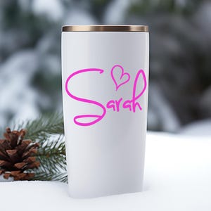 May include: White travel mug with a gold lid and a pink cursive design that says "Sarah" with a heart above the name.