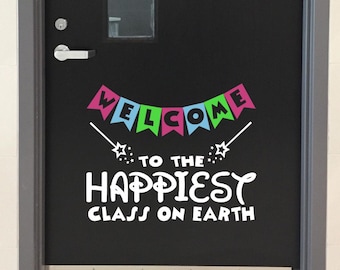 Puede incluir: Una puerta negra con una calcomanía de vinilo blanco que dice "Bienvenido a la clase más feliz de la Tierra". La calcomanía presenta una pancarta colorida con la palabra "Bienvenido" y estrellas con varitas.