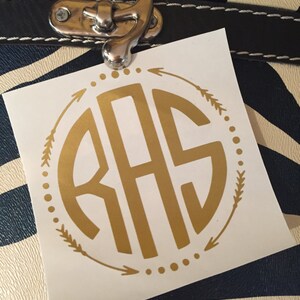 May include: A white sticker with a gold monogram of the letters "RAS" in a circle with arrows and dots around it.
