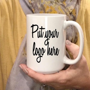 May include: White ceramic mug with a black handwritten message that says "Put your logo here".