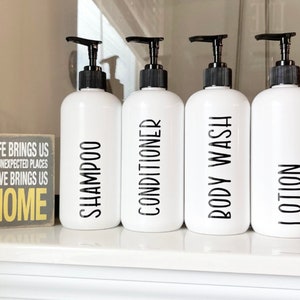 May include: Four white pump bottles with black labels and black pump tops. The labels read "Shampoo", "Conditioner", "Body Wash", and "Lotion".