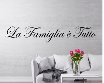 May include: A white couch with a throw blanket and a vase of pink flowers. The wall behind the couch has a black cursive inscription that reads "La Famiglia è Tutto".
