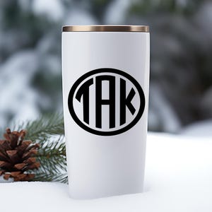 May include: White travel mug with a black oval monogram that says "TAK" on it.