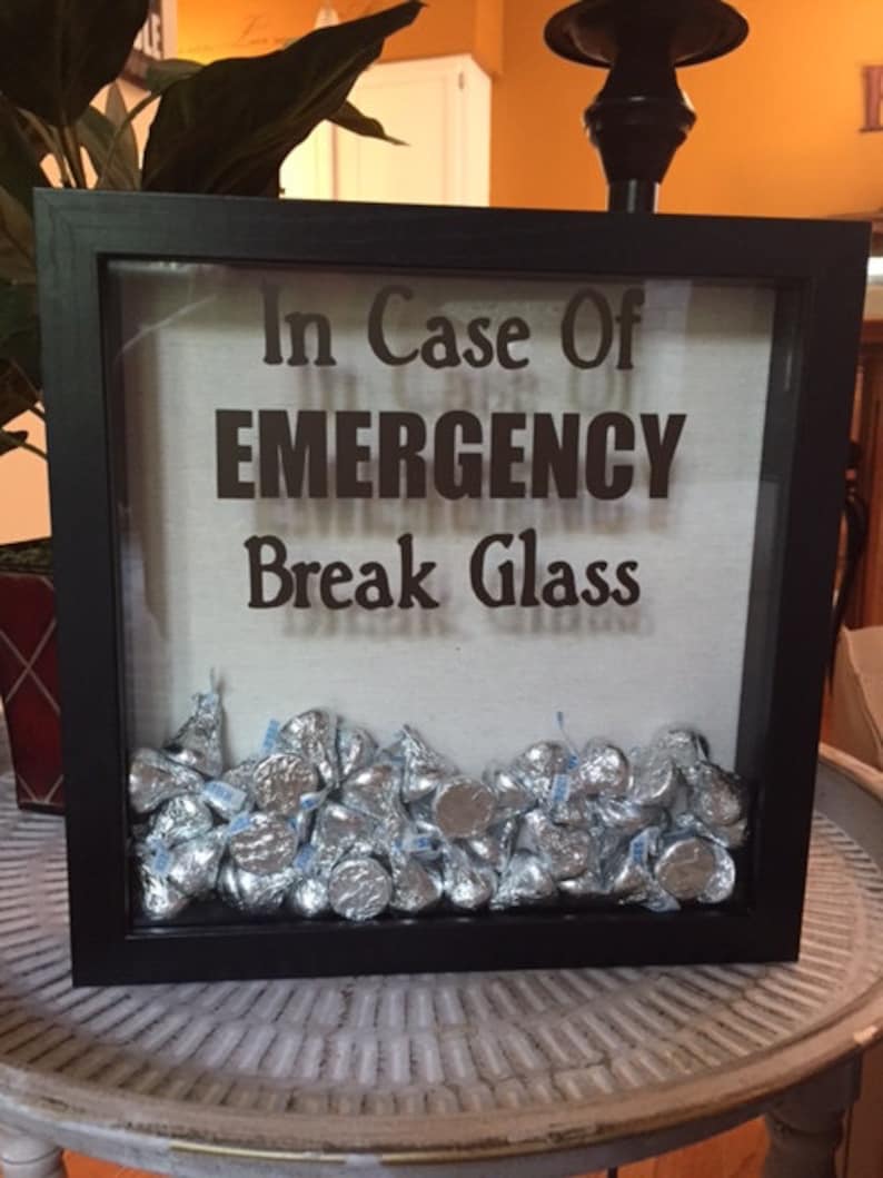May include: A black shadow box with the text "In Case Of EMERGENCY Break Glass" and filled with silver foil-wrapped chocolate kisses.